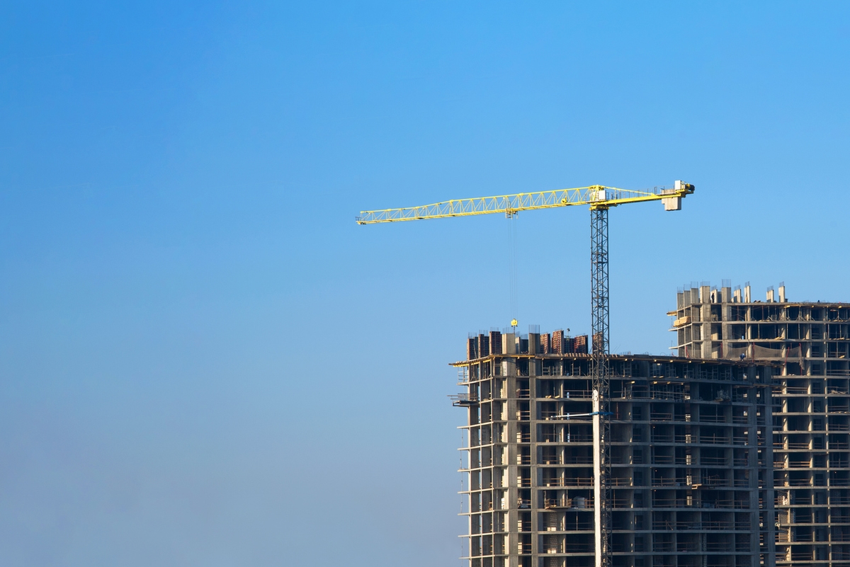 Tower cranes constructing a new residential building at a construction site against blue sky. Renovation program, development, concept of the buildings industry.