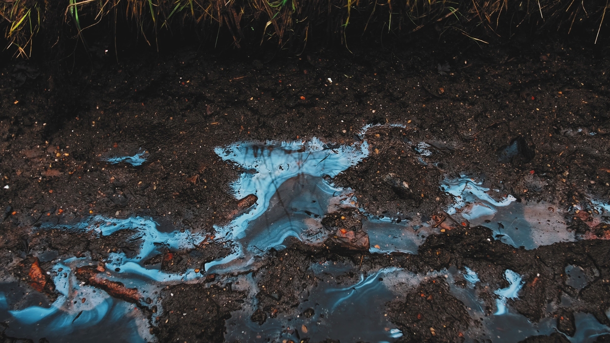 Smudges of Toxic Industrial Liquid Chemical Pollutant Visible on Surface of Rain Water Puddles on Muddy Ground Road