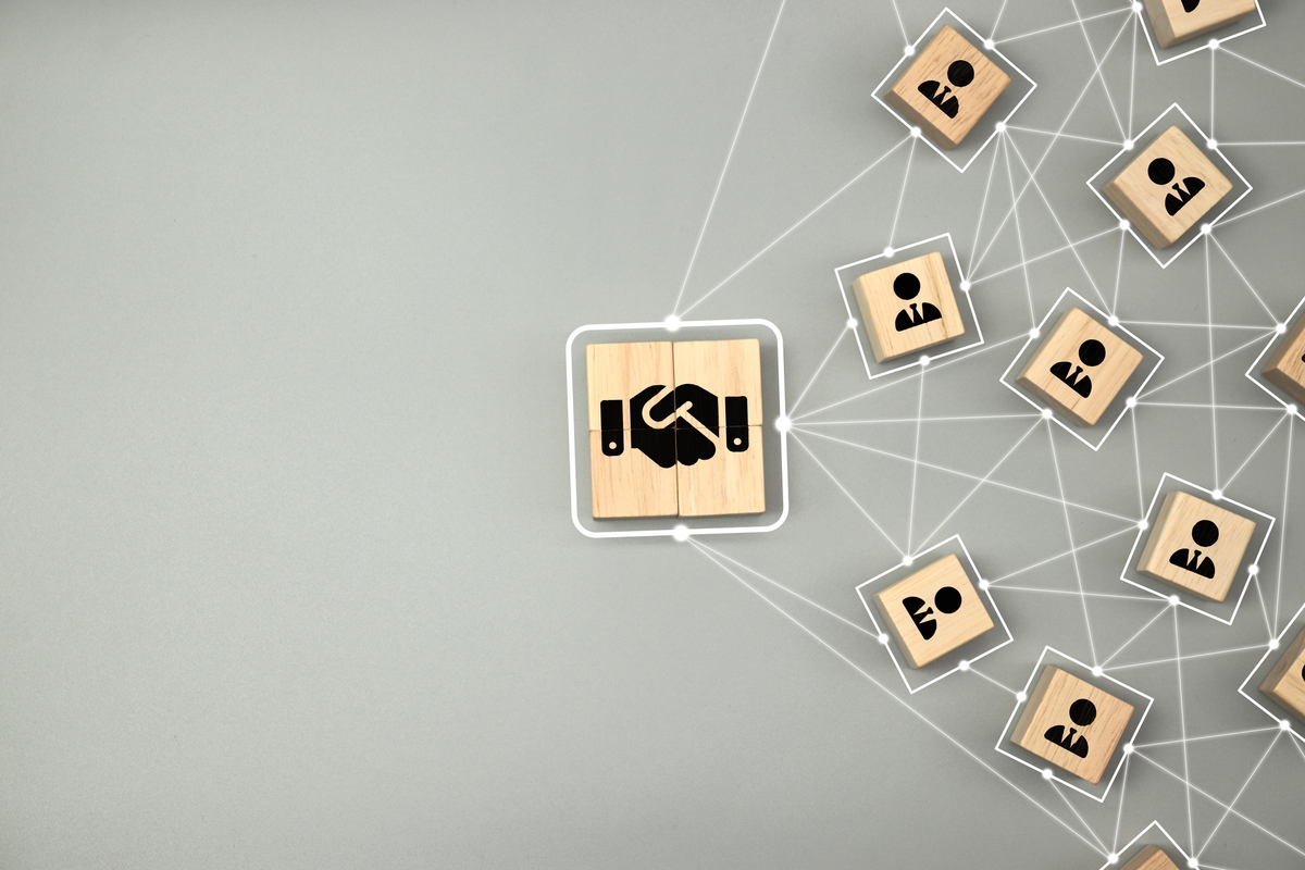 Hand shake icon on wooden cube block which connection with human icon for business deal and agreement concept.
