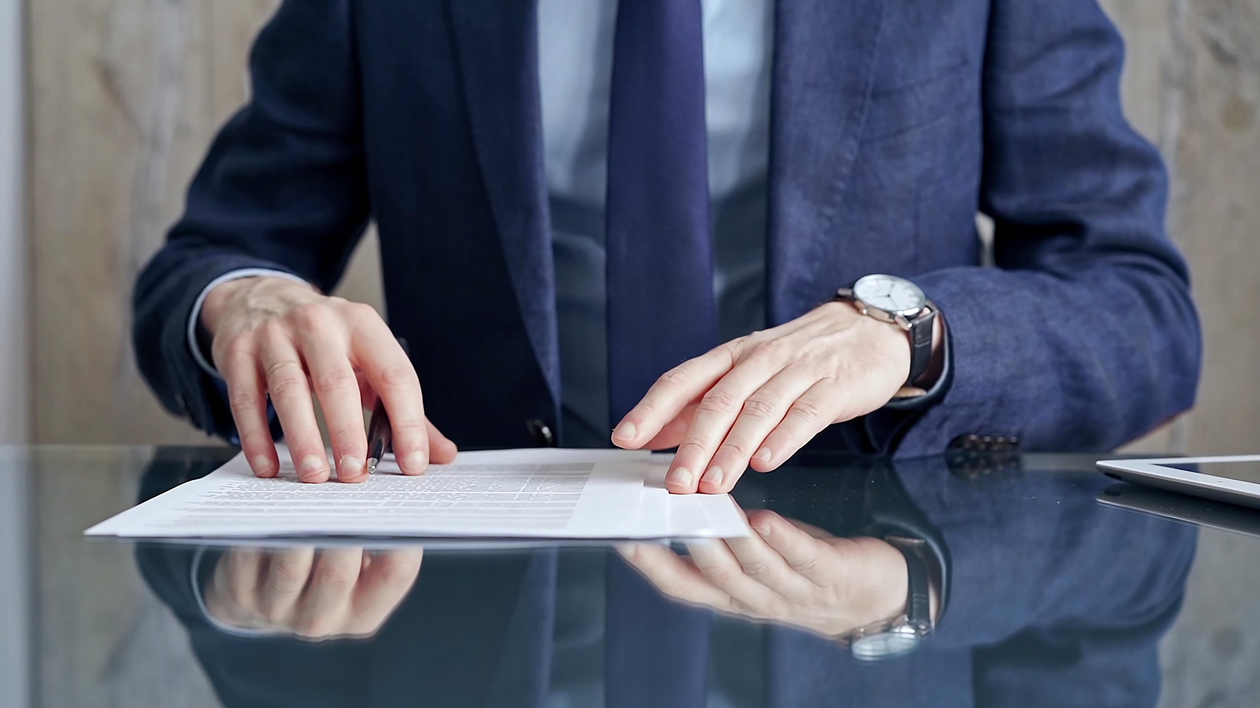 Businessman reviewing documents at office desk. Close-up of a professional man&#8217;s hands examining paperwork with pen and tablet in sight. Business people concept