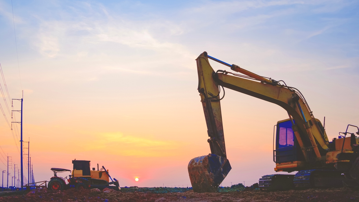 Silhouette of excavator and bulldozer tractor parked after work in land filling area for industrial factory construction site at sunset time