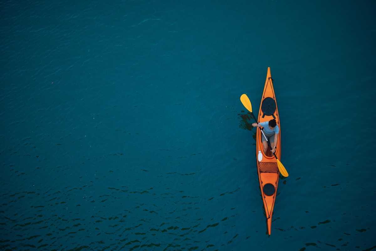 Man in Orange Kayak Paddling on Calm Blue Water, Top-Down View
