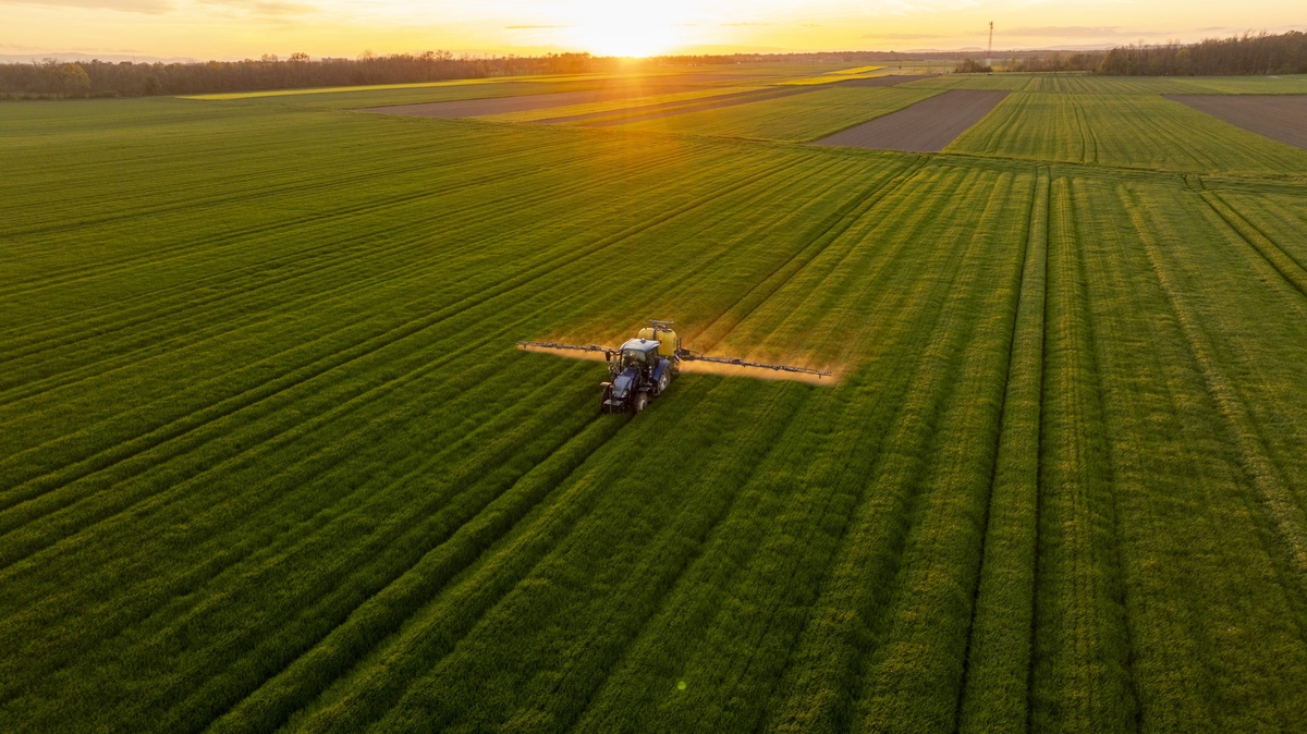 Tractor Fertilizing Verdant Agricultural Field During Golden Sunset