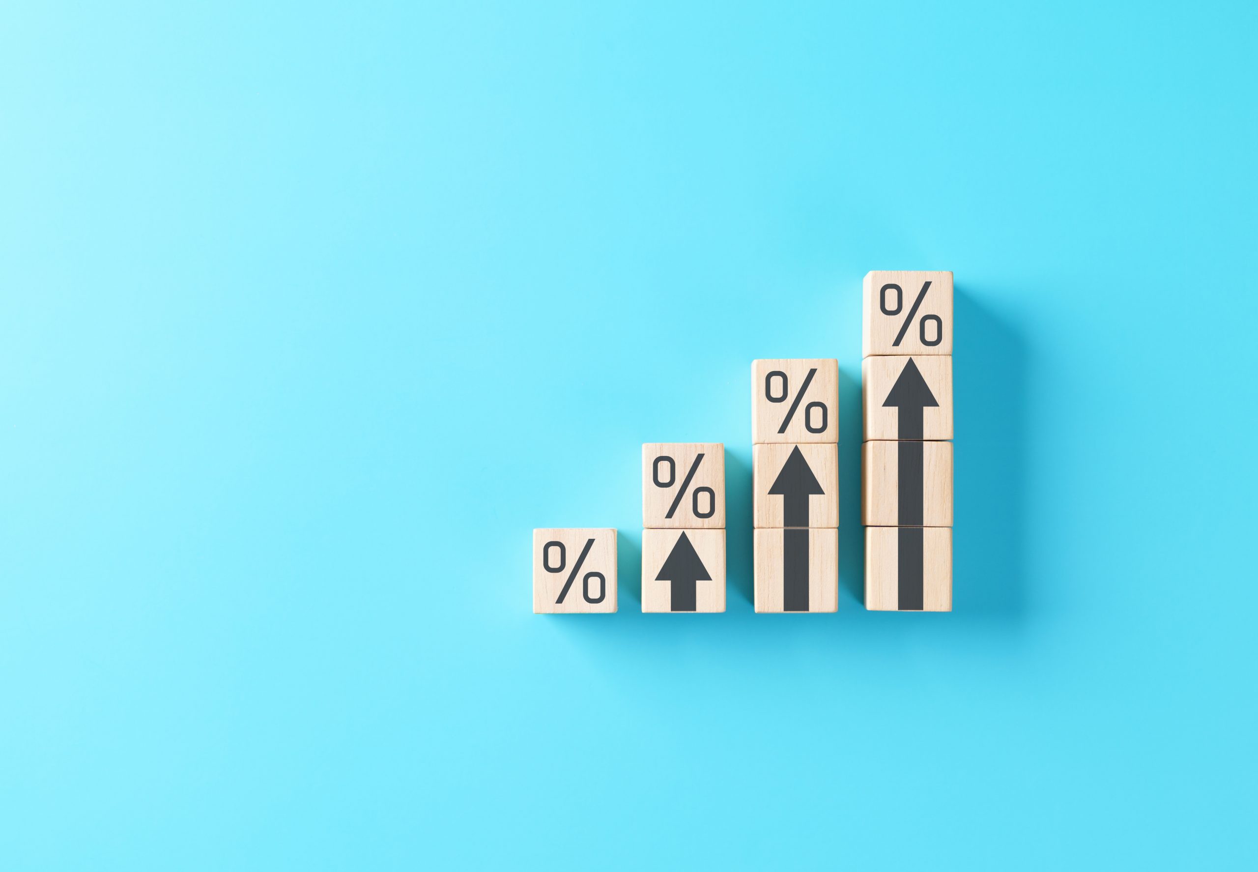 Rising interest rate or growth percentage concept shown with wooden blocks and upward arrows on blue background, symbolizing financial increase, profitability, profit, economy and return on investment
