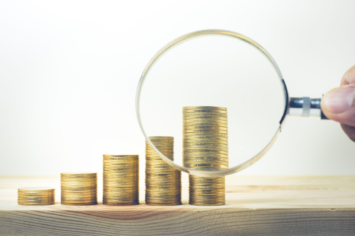 Male hand holding magnifying glass with coin stacked